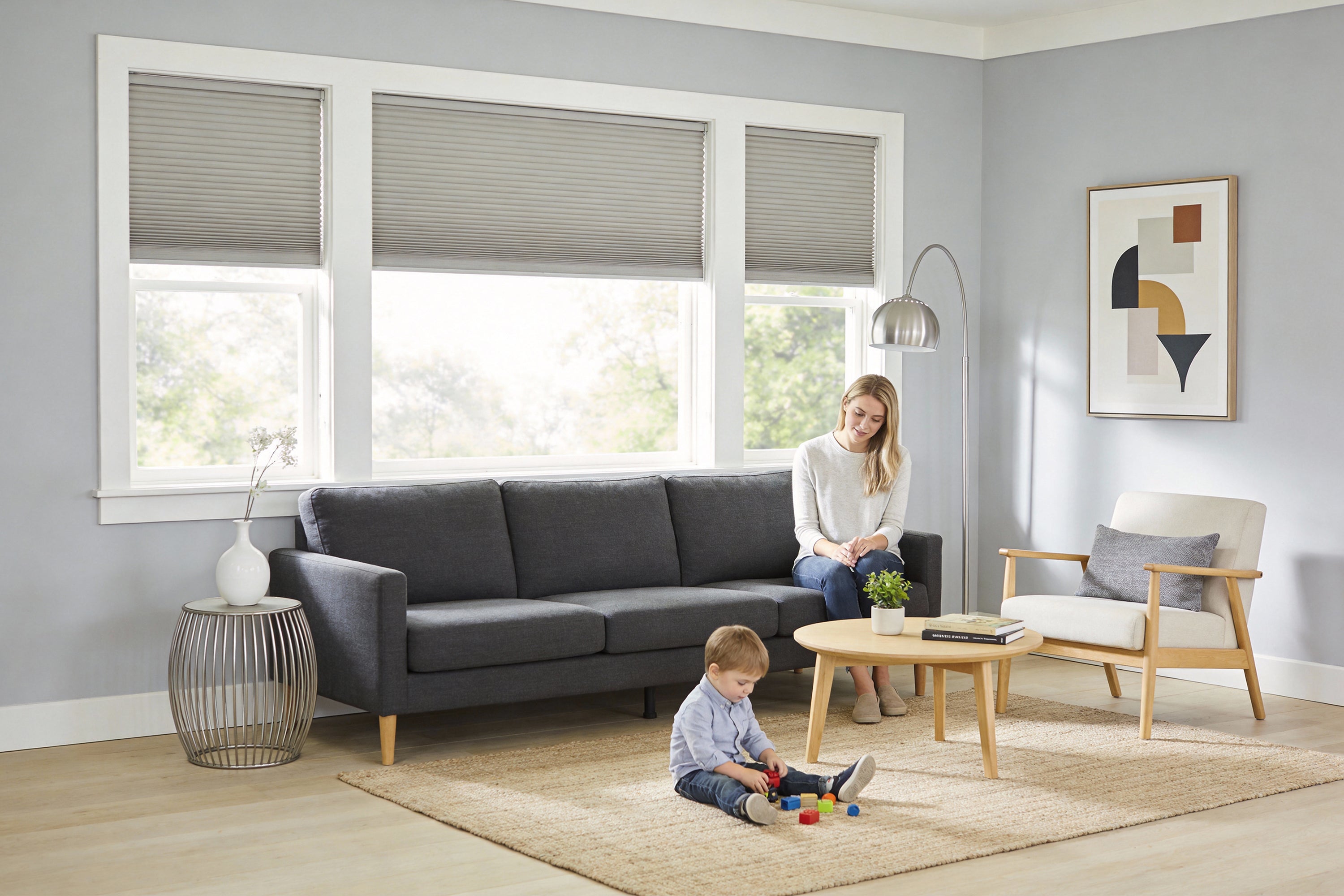 a living room featuring three cordless cellular shades in a neutral gray, providing a safe and stylish window covering solution for families