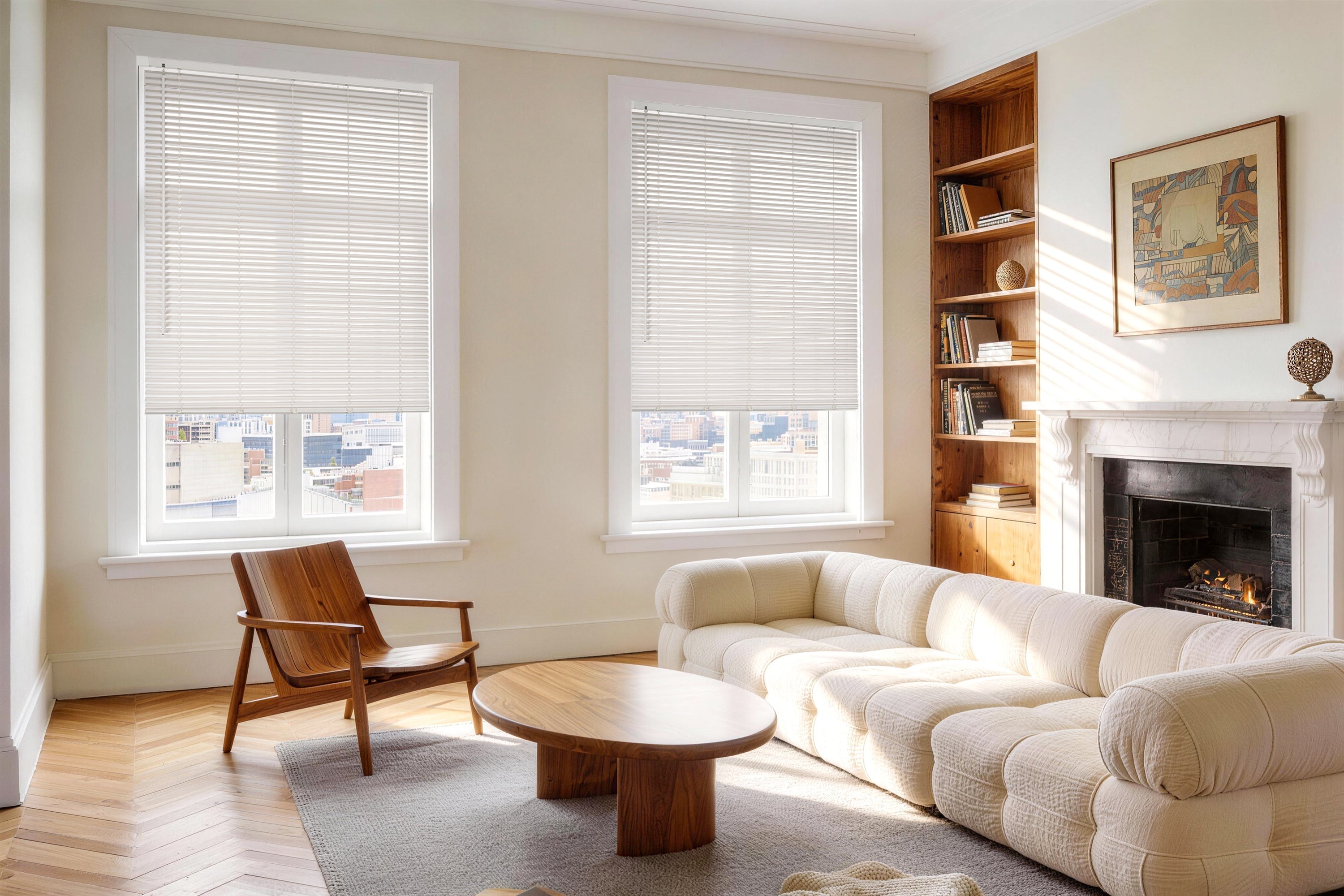 white horizontal blinds are partially lowered over two large windows in a bright, modern living room, filtering the natural sunlight into the space