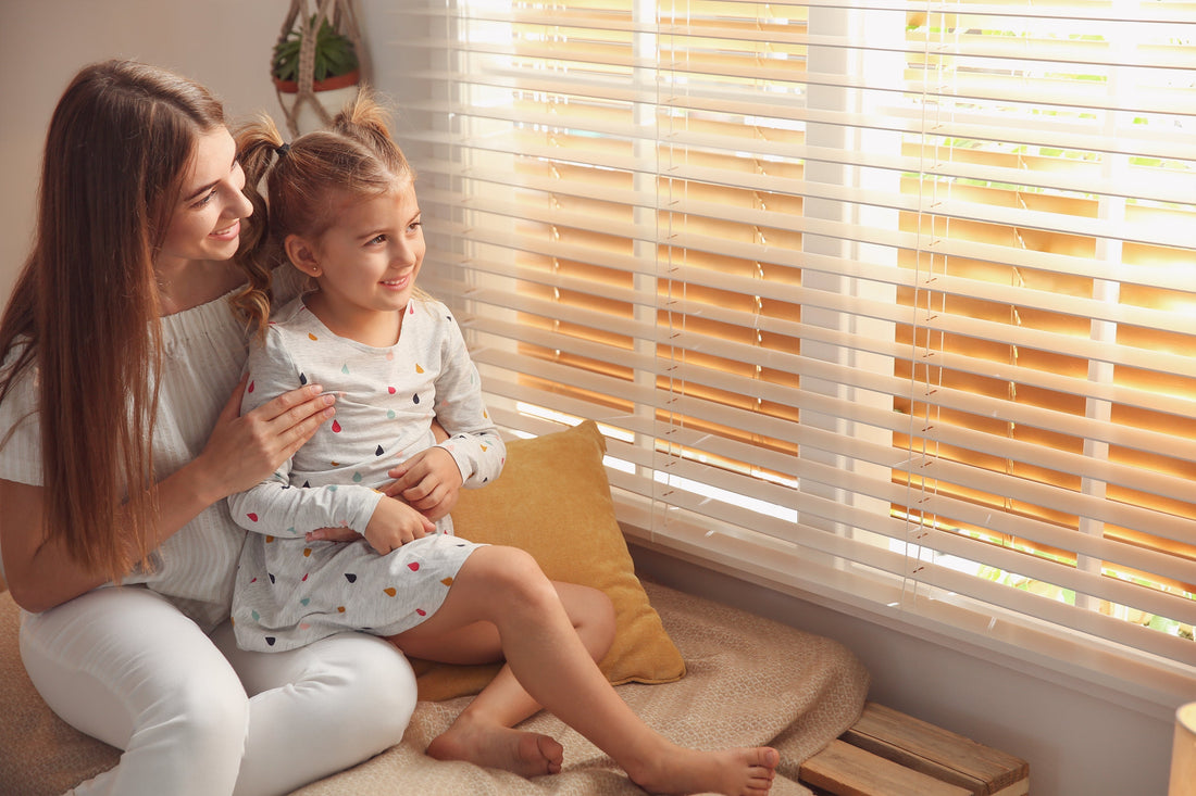 a woman and a kid sitting beside white faux-wood blinds