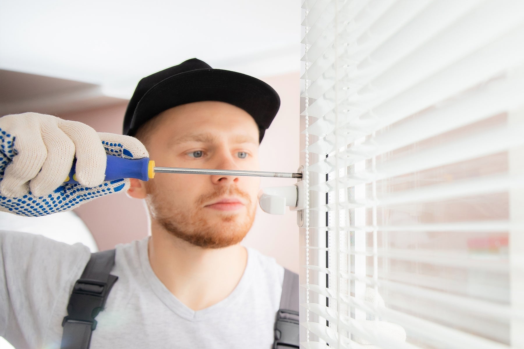 a man using a screw driver to fix white mini blinds