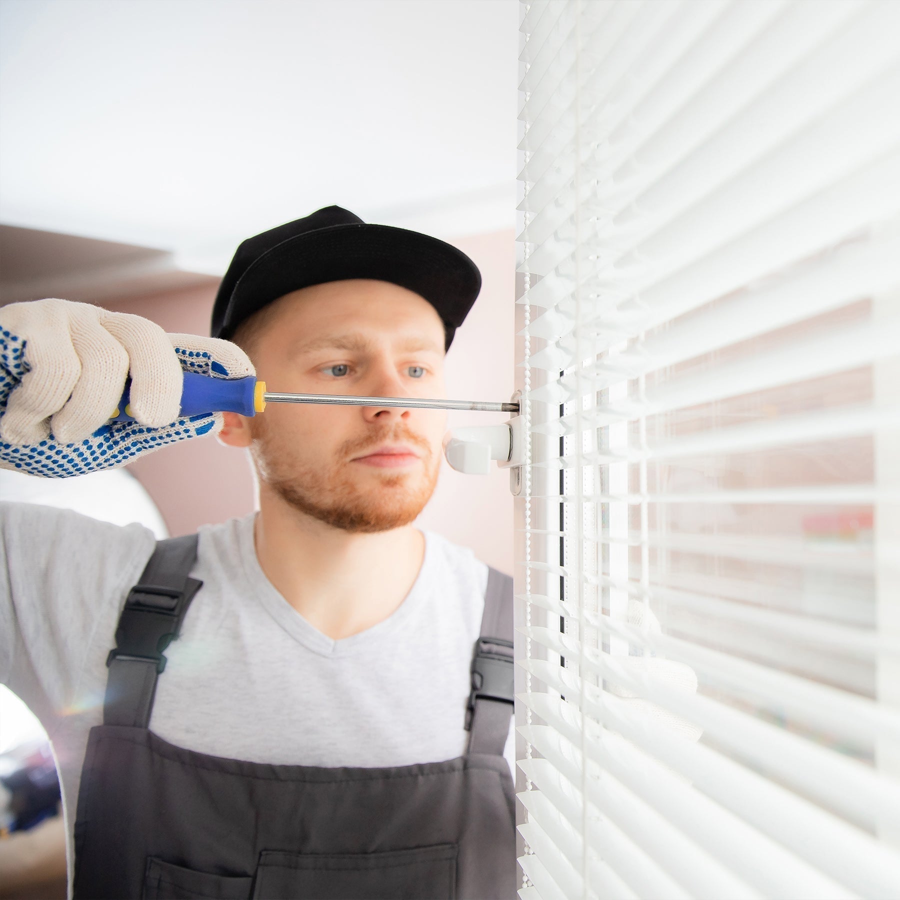 a man using a screw driver to fix white mini blinds