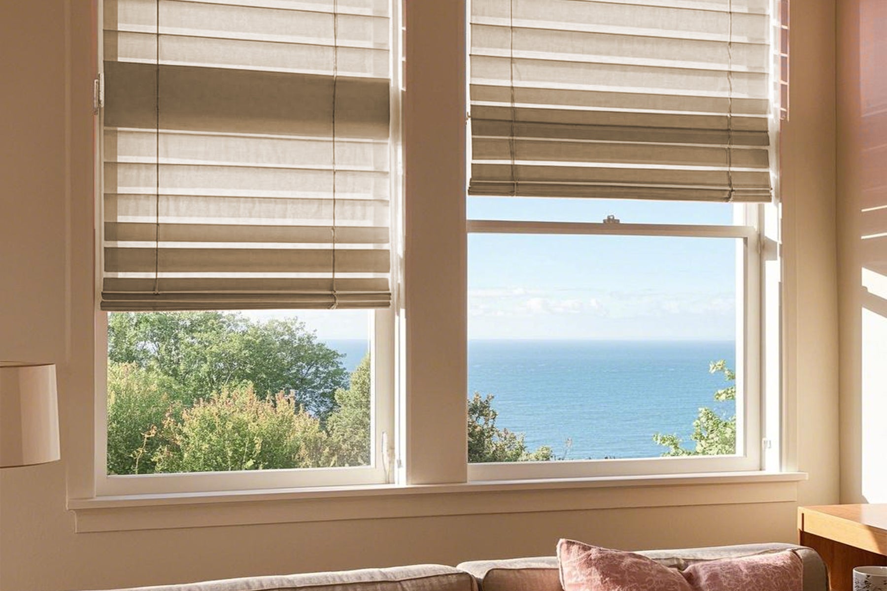 beige roman shades on a large window, afternoon sun, sea shimmering